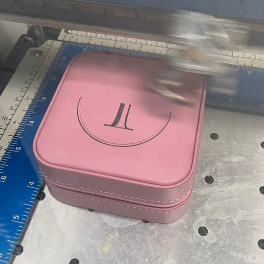 Pink leatherette 4x4 travel jewelry box being laser engraved with a monogram