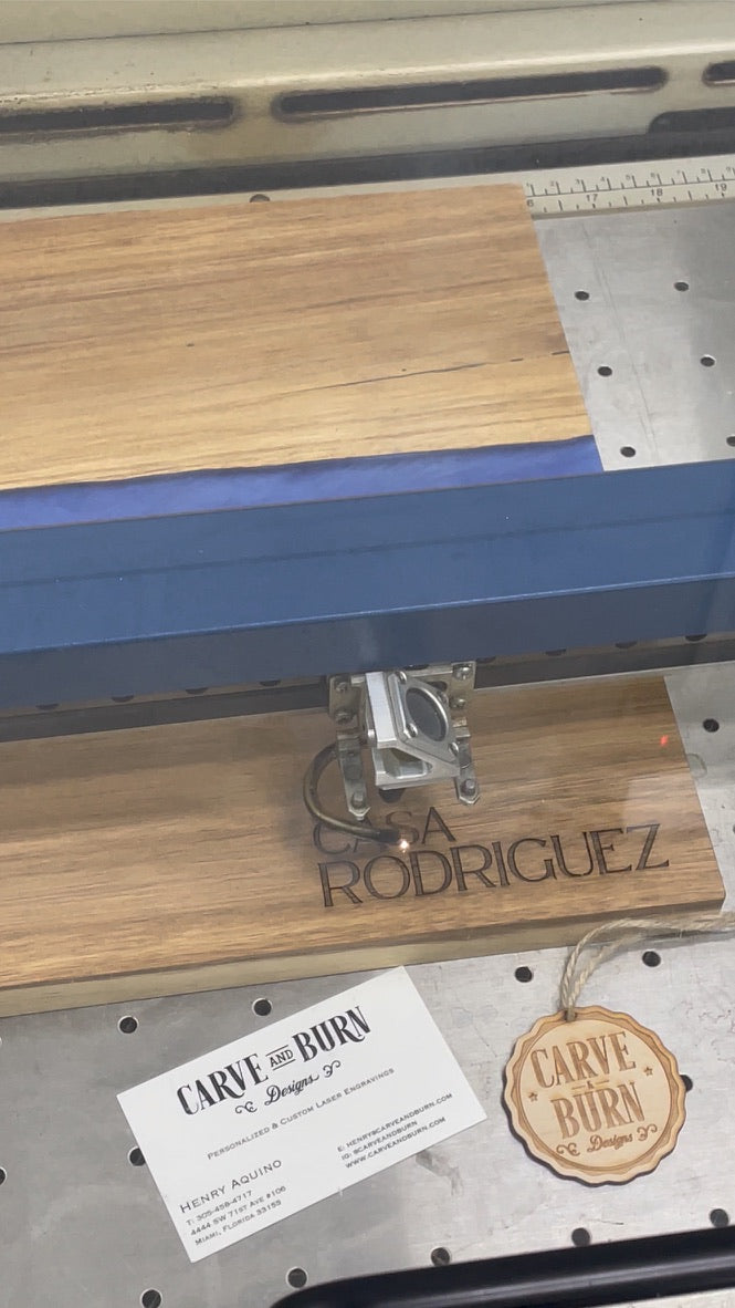 Acacia and blue resin board engraved Casa Rodriguez on the laser bed with a Carve & Burn card