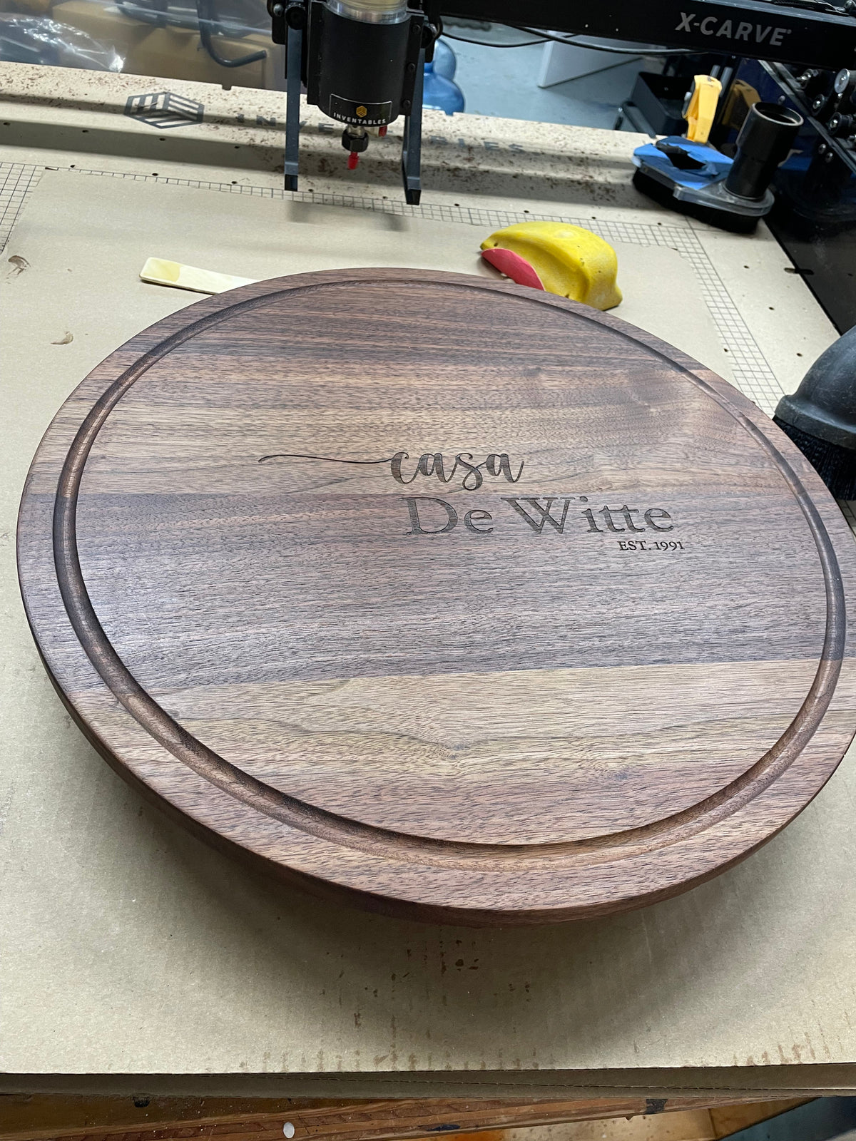 20 inch round black walnut serving board engraved with a family name on the bench