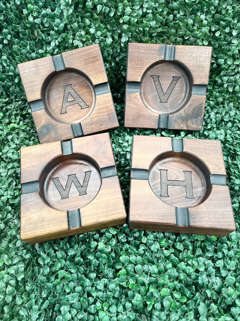 Four black walnut ashtrays engraved with initials A, V, W and H on a green backdrop
