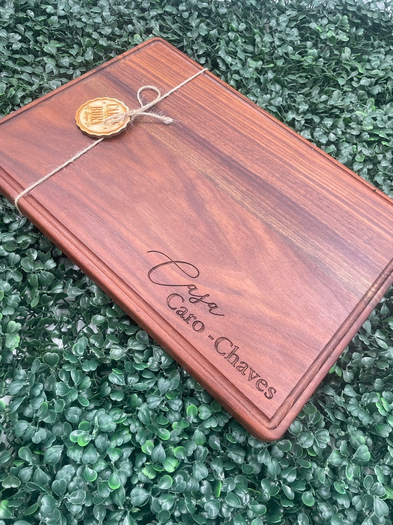 Black walnut cutting board engraved with a script family name, tied with twine and a tag