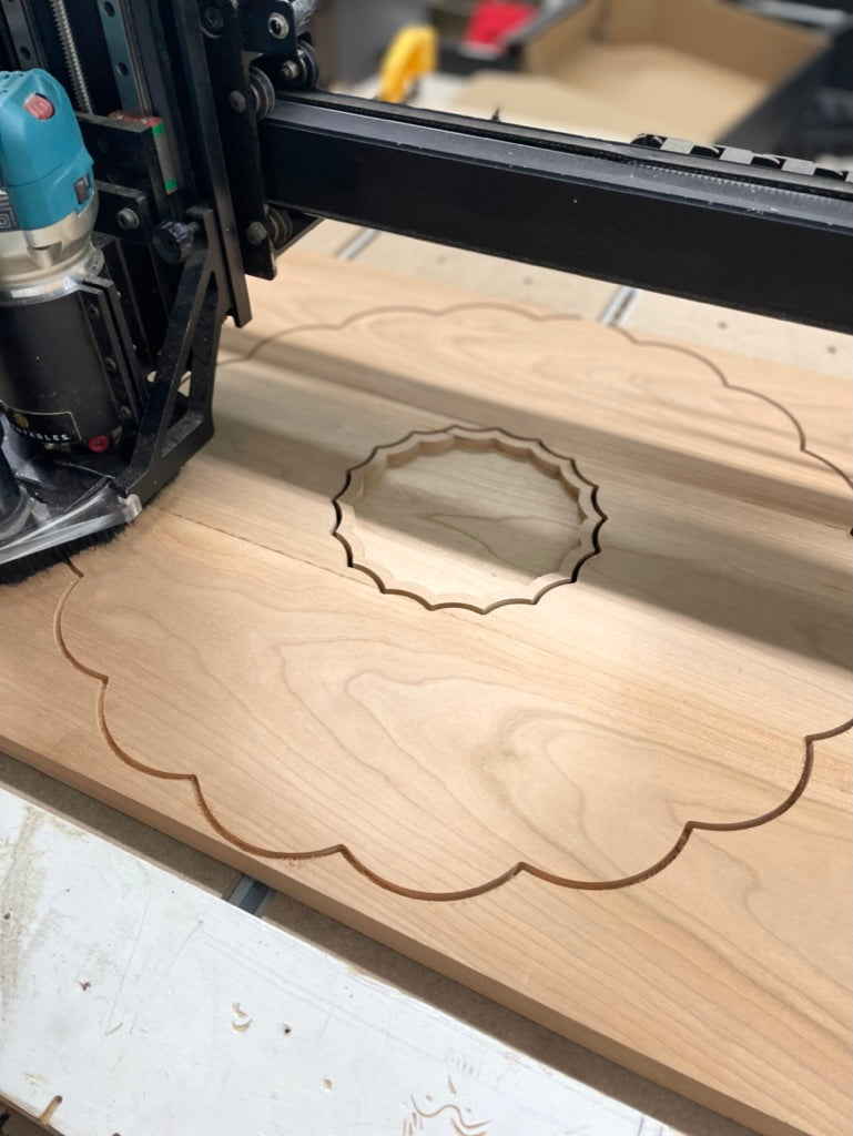 CNC machine cutting the scalloped outline of a cherry clamshell charcuterie board