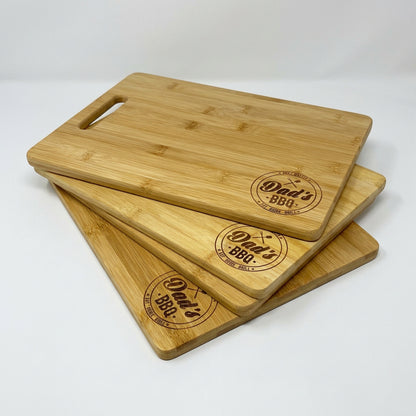 Three Dad's BBQ bamboo cutting boards stacked, engraved with the Dad's BBQ badge