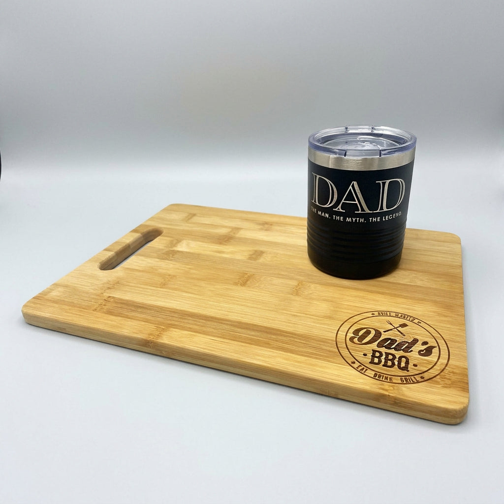 Dad's BBQ bamboo cutting board shown with an engraved black Dad lowball tumbler