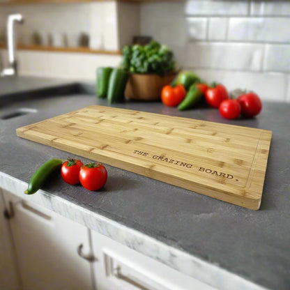The Grazing Board large bamboo serving board engraved with a name, styled in a kitchen with tomatoes